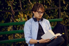 Портрет красивого молодого человека в eyeglasses и наушниках, прочитал книгу снаружи, изолированный на городской предпосылке парк стоковое фото Портрет красивого молодого человека в eyeglasses и наушниках, прочитал книгу снаружи, изолированный на городской предпосылке парк стоковое фото