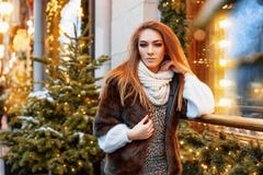 Портрет красивой молодой женщины которая представляет на улице около элегантно украшенного окна рождества, праздничное настроение стоковое фото Портрет красивой молодой женщины которая представляет на улице около элегантно украшенного окна рождества, праздничное настроение стоковое фото