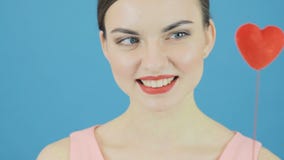 Портрет крупного плана изумительного брюнет с меньшим красным сердцем в руке на голубой предпосылке в студии сток-видео Портрет крупного плана изумительного брюнет с меньшим красным сердцем в руке на голубой предпосылке в студии сток-видео