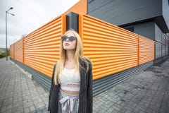 Портрет крупного плана милой усмехаясь маленькой модельной девушки в striped куртке и солнечных очках представляя около серого ри стоковое фото rf Портрет крупного плана милой усмехаясь маленькой модельной девушки в striped куртке и солнечных очках представляя около серого ри стоковое фото rf