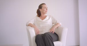 Портрет крупного плана пожилой кавказской женщины брюнета сидя в кресле в белой квартире внутри помещения видеоматериал Портрет крупного плана пожилой кавказской женщины брюнета сидя в кресле в белой квартире внутри помещения видеоматериал