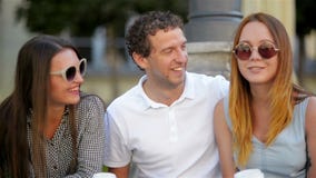 Портрет крупного плана 3 усмехаясь друзей сидя с чашками кофе Outdoors и говоря во время временени девушки 2 сток-видео Портрет крупного плана 3 усмехаясь друзей сидя с чашками кофе Outdoors и говоря во время временени девушки 2 сток-видео