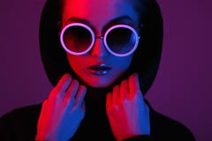 Портрет маленькой девочки моды в черном свитере с клобуком и круглыми солнечными очками в красном и голубом неоновом свете в стоковое фото rf Портрет маленькой девочки моды в черном свитере с клобуком и круглыми солнечными очками в красном и голубом неоновом свете в стоковое фото rf