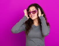 Портрет молодой женщины красивый, представляя на фиолетовой предпосылке, длинное вьющиеся волосы, солнечные очки в сердце формиру стоковые изображения Портрет молодой женщины красивый, представляя на фиолетовой предпосылке, длинное вьющиеся волосы, солнечные очки в сердце формиру стоковые изображения