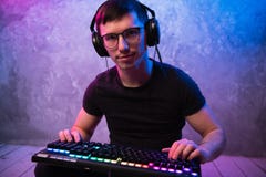 Портрет молодого красивого pro gamer сидя на поле с клавиатурой в неоновой покрашенной комнате стоковое изображение Портрет молодого красивого pro gamer сидя на поле с клавиатурой в неоновой покрашенной комнате стоковое изображение