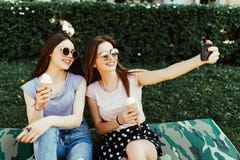 Портрет 2 молодых милых женщин стоя совместно ел мороженое и принимающ фото selfie на камере в улице лета стоковая фотография Портрет 2 молодых милых женщин стоя совместно ел мороженое и принимающ фото selfie на камере в улице лета стоковая фотография