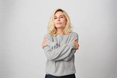 Портрет себя молодого белокурого объятия девушки, носит вскользь серый свитер и чувствует удобным и теплым Стоковое Изображение Портрет себя молодого белокурого объятия девушки, носит вскользь серый свитер и чувствует удобным и теплым Стоковое Изображение