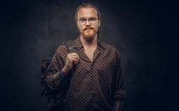 Портрет студента битника redhead в стеклах одетых в коричневой рубашке, владениях рюкзак, представляя на студии стоковое фото Портрет студента битника redhead в стеклах одетых в коричневой рубашке, владениях рюкзак, представляя на студии стоковое фото