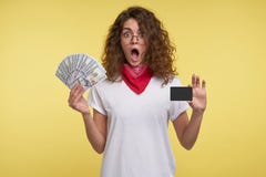 Портрет счастливой молодой женщины с вьющиеся волосы брюнета, держащ наличные деньги и тележку кредита в руках, изолированных све стоковая фотография rf Портрет счастливой молодой женщины с вьющиеся волосы брюнета, держащ наличные деньги и тележку кредита в руках, изолированных све стоковая фотография rf
