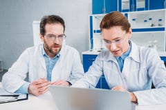 портрет ученых в пальто и eyeglasses лаборатории работая на компьтер-книжке совместно на рабочем месте стоковые фотографии rf портрет ученых в пальто и eyeglasses лаборатории работая на компьтер-книжке совместно на рабочем месте стоковые фотографии rf