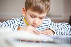 Прелестные 7 лет мальчика сидя на столе с книгой и записью стоковое фото rf Прелестные 7 лет мальчика сидя на столе с книгой и записью стоковое фото rf