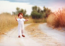 Прелестный ребёнок малыша redhead в комбинезоне бежать вдоль сельской дороги лета в sunburned поле стоковое фото Прелестный ребёнок малыша redhead в комбинезоне бежать вдоль сельской дороги лета в sunburned поле стоковое фото