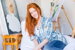 Привлекательная счастливая женщина сидя на белой погремушке в художественной мастерской стоковая фотография Привлекательная счастливая женщина сидя на белой погремушке в художественной мастерской стоковая фотография