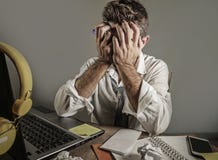 Привлекательный унылый и отчаянный человек внутри теряет галстук смотря грязная и подавленная работа на столе портативного компью стоковое фото Привлекательный унылый и отчаянный человек внутри теряет галстук смотря грязная и подавленная работа на столе портативного компью стоковое фото