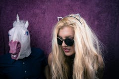 Причудливая молодая женщина в солнечных очках и ушах киски целуя счастливый единорога стоковое изображение Причудливая молодая женщина в солнечных очках и ушах киски целуя счастливый единорога стоковое изображение