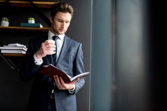 Приятный уверенно щетиненнсяый парень стоит в офисе с кофе стоковые изображения rf Приятный уверенно щетиненнсяый парень стоит в офисе с кофе стоковые изображения rf