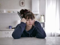 Пробуренная женщина сидя с дистанционным управлением на запачканной предпосылке кухни стоковые изображения Пробуренная женщина сидя с дистанционным управлением на запачканной предпосылке кухни стоковые изображения