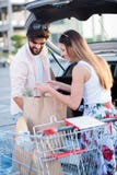 Продуктовые сумки счастливых молодых пар нагружая в автомобиль стоковое изображение rf Продуктовые сумки счастливых молодых пар нагружая в автомобиль стоковое изображение rf