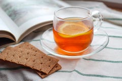 Прозрачная чашка чаю с лимоном, crispbread рож, книгой, естественным светом, завтраком стоковые фотографии rf Прозрачная чашка чаю с лимоном, crispbread рож, книгой, естественным светом, завтраком стоковые фотографии rf