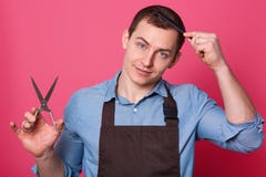 Профессиональный мужской парикмахер держит ножницы в руке, расчесывает, одетый в голубой рубашке и коричневой рисберме, работы на стоковые фото Профессиональный мужской парикмахер держит ножницы в руке, расчесывает, одетый в голубой рубашке и коричневой рисберме, работы на стоковые фото