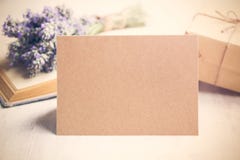 Пустая приветствуя карточка kraft перед букетом лаванды, обернутым подарком и старой книгой над белой деревянной предпосылкой сбо Стоковое Изображение RF Пустая приветствуя карточка kraft перед букетом лаванды, обернутым подарком и старой книгой над белой деревянной предпосылкой сбо Стоковое Изображение RF