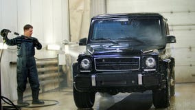 Работник в автоматическом обслуживании моет роскошный автомобиль шлангами воды, backlight Работник в автоматическом обслуживании моет роскошный автомобиль шлангами воды, backlight