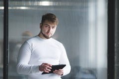 Работник офиса стоя с таблеткой в его руках на фоне стены и смотря камеру стоковое изображение Работник офиса стоя с таблеткой в его руках на фоне стены и смотря камеру стоковое изображение