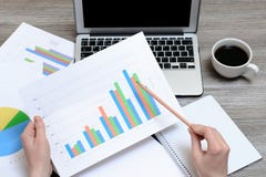 Работник смотря графики Взгляд сверху на руках держа диаграммы, компьтер-книжку, чашку кофе, рабочее место рабочего места, прогре стоковое фото rf Работник смотря графики Взгляд сверху на руках держа диаграммы, компьтер-книжку, чашку кофе, рабочее место рабочего места, прогре стоковое фото rf