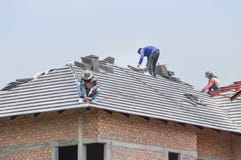 Работники устанавливая конкретные плитки на крышу пока настилающ крышу дом стоковое фото rf Работники устанавливая конкретные плитки на крышу пока настилающ крышу дом стоковое фото rf