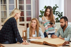 Разнообразные multiracial студенты тратя часы досуга в библиотеке с большой старой книгой стоковые фотографии rf Разнообразные multiracial студенты тратя часы досуга в библиотеке с большой старой книгой стоковые фотографии rf