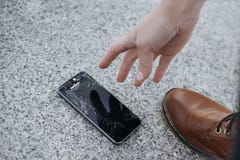 Расстроенный молодой человек сидит и держит сломленный смартфон с треснутым стеклянным экраном стоковое изображение rf Расстроенный молодой человек сидит и держит сломленный смартфон с треснутым стеклянным экраном стоковое изображение rf