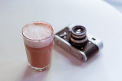 Розовое cappucciono кофе хипстера на белой таблице со старомодной ретро камерой фото фильма стиля стоковое фото rf Розовое cappucciono кофе хипстера на белой таблице со старомодной ретро камерой фото фильма стиля стоковое фото rf