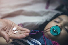 Рука держа таблетки медицины над азиатским ребенк с pacifier в ее рте стоковое фото rf Рука держа таблетки медицины над азиатским ребенк с pacifier в ее рте стоковое фото rf