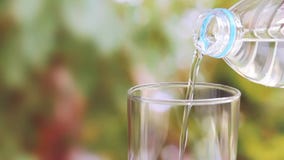 Рука женщины держа бутылку с водой и лить ясной питьевой воды в стекло на запачканной зеленой предпосылке природы сток-видео Рука женщины держа бутылку с водой и лить ясной питьевой воды в стекло на запачканной зеленой предпосылке природы сток-видео