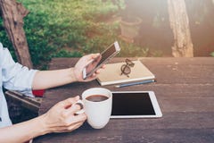 Рука женщины держа телефон и используя телефон на таблице в саде стоковое изображение Рука женщины держа телефон и используя телефон на таблице в саде стоковое изображение