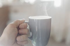 Рука человека держа чашку горячих черного кофе или americano с запачканным естественной солнечным светом предпосылки и утра стоковые изображения rf Рука человека держа чашку горячих черного кофе или americano с запачканным естественной солнечным светом предпосылки и утра стоковые изображения rf