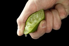 Рука человека сжимает сок от половины известки Сочное падение вися вниз стоковые фото Рука человека сжимает сок от половины известки Сочное падение вися вниз стоковые фото