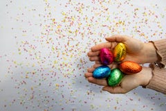 Руки женщины держа красочные пасхальные яйца шоколада с белой предпосылкой и красочный запачканный confetti стоковая фотография Руки женщины держа красочные пасхальные яйца шоколада с белой предпосылкой и красочный запачканный confetti стоковая фотография