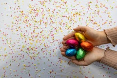 Руки женщины держа красочные пасхальные яйца шоколада с белой предпосылкой и красочный запачканный confetti стоковая фотография rf Руки женщины держа красочные пасхальные яйца шоколада с белой предпосылкой и красочный запачканный confetti стоковая фотография rf