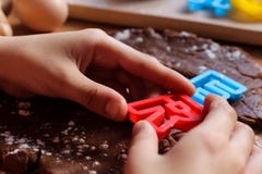 Руки мальчика детенышей отрезали печенья от сырцового теста шоколада на деревянном столе с красочными письмами Варить традиционну стоковые фотографии rf Руки мальчика детенышей отрезали печенья от сырцового теста шоколада на деревянном столе с красочными письмами Варить традиционну стоковые фотографии rf