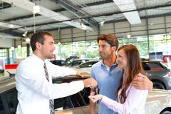 Руки продавца автомобилей над ключом автомобиля в автосалоне к cus стоковое фото rf Руки продавца автомобилей над ключом автомобиля в автосалоне к cus стоковое фото rf