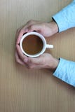 руки человека для того чтобы обнять белую кофейную чашку на коричневой таблице и стоковая фотография руки человека для того чтобы обнять белую кофейную чашку на коричневой таблице и стоковая фотография