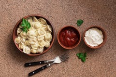 Русские вареники мяса pelmeni еды со сметаной и кетчуп аранжированными в ряд на коричневой каменной предпосылке Надземный взгляд, стоковое фото rf Русские вареники мяса pelmeni еды со сметаной и кетчуп аранжированными в ряд на коричневой каменной предпосылке Надземный взгляд, стоковое фото rf