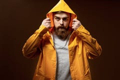 Рыжеволосый парень с бородой и усиком одетыми в серой футболке и желтой куртке с клобуком представляет на коричневом цвете стоковая фотография rf Рыжеволосый парень с бородой и усиком одетыми в серой футболке и желтой куртке с клобуком представляет на коричневом цвете стоковая фотография rf