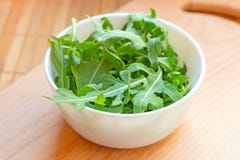 Свежие здоровые зеленые листья arugula в белом шаре на светлой деревянной предпосылке стоковая фотография rf Свежие здоровые зеленые листья arugula в белом шаре на светлой деревянной предпосылке стоковая фотография rf