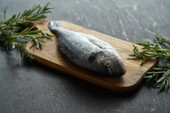 Свежие сырцовые рыбы dorada с розмариновым маслом, перцем и солью на деревянной доске и черной таблице стоковые изображения Свежие сырцовые рыбы dorada с розмариновым маслом, перцем и солью на деревянной доске и черной таблице стоковые изображения