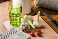 Свежий молодой чеснок, нож, небольшие томаты и зеленое стекло воды на кухонном столе стоковая фотография rf Свежий молодой чеснок, нож, небольшие томаты и зеленое стекло воды на кухонном столе стоковая фотография rf