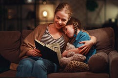 Семья перед идти положить мать в постель читает к ее книге дочери ребенка около лампы в вечере стоковые изображения rf Семья перед идти положить мать в постель читает к ее книге дочери ребенка около лампы в вечере стоковые изображения rf