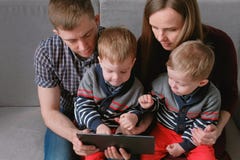 Семья с таблеткой Мама, папа и 2 близнеца сыновьей смотря таблетку сидя в софе стоковое изображение rf Семья с таблеткой Мама, папа и 2 близнеца сыновьей смотря таблетку сидя в софе стоковое изображение rf