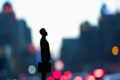 Силуэт бизнесмена держа портфель с запачканным городом освещает за им Стоковое Фото Силуэт бизнесмена держа портфель с запачканным городом освещает за им Стоковое Фото